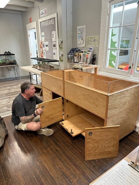 person sitting on the floor in front of the turtle enclosure putting the cabinet doors on