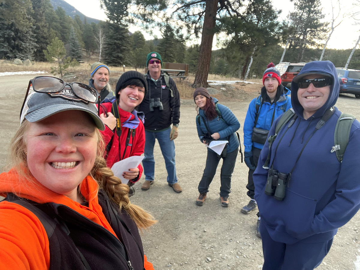 Seven people taking a selfie in a dirt parking lot.