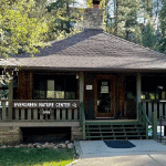 Old house with sign "Evergreen Nature Center" with pine trees in the background